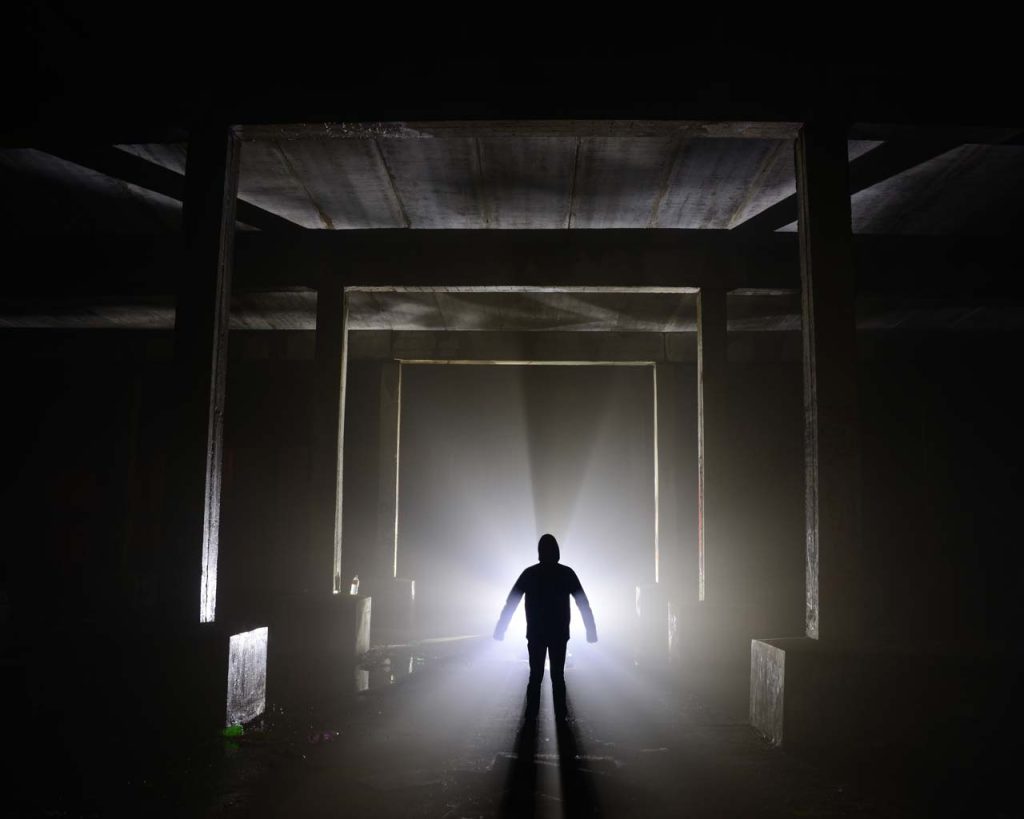A man standing in a dark warehouse with light streaming from outside